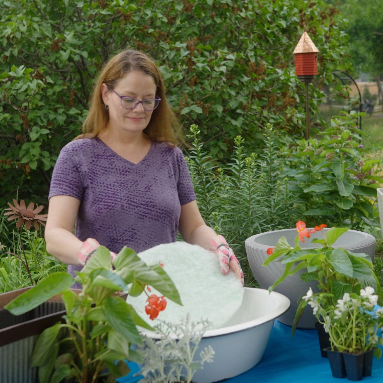Woman preparing a round planter with a Better Than Rocks drainage insert in a backyard garden, surrounded by flowers and pots for container gardening.