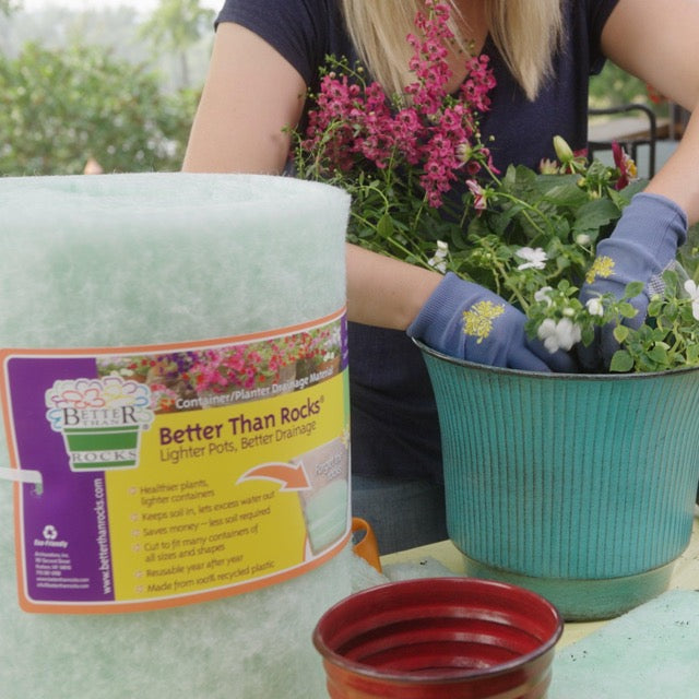 Gardener planting flowers in a container lined with Better Than Rocks Jumbo Roll drainage material, with tools and extra inserts on a patio work table.