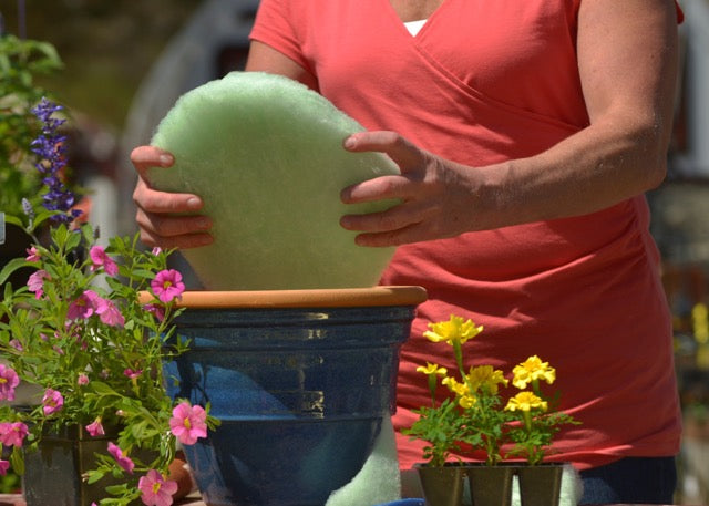 A gardener placing a Better Than Rocks eco-friendly drainage sheet into a blue planter, surrounded by blooming flowers — demonstrating sustainable container gardening.