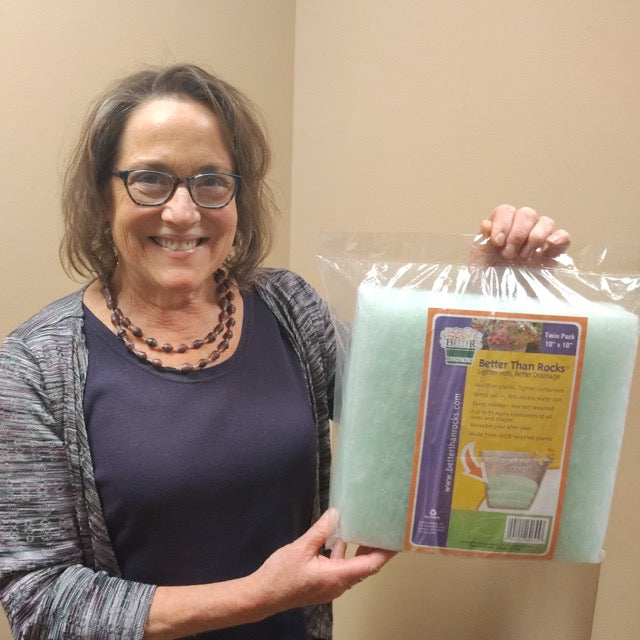 Sarah Atkins, creator of Better Than Rocks, smiling and holding a packaged version of the eco-friendly planter drainage product made from recycled plastic.
