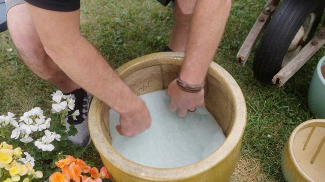 Hands placing Better Than Rocks drainage material into the base of a large planter.
